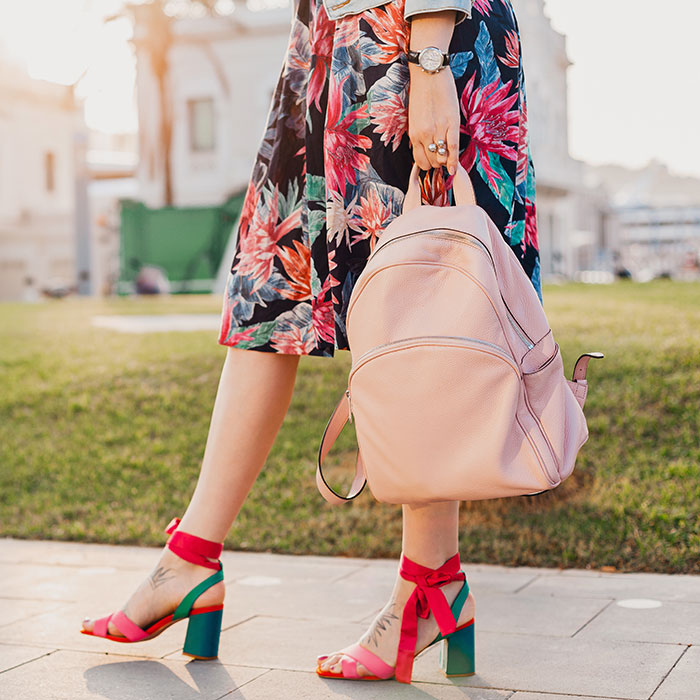 close-up-details-legs-pink-sandals-stylish-woman-walking-city-street-printed-colorful-skirt-holding-pink-leather-backpack